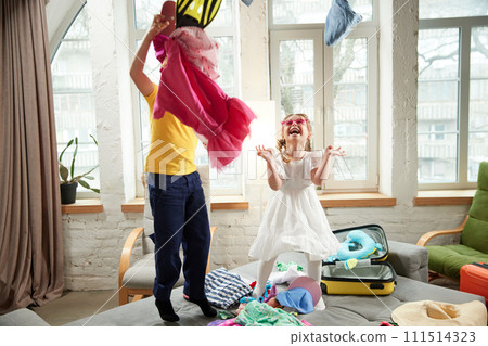 Two kids, boy and girl jumping on bed and having fun throwing things in different directions when preparing for trip. Two kids, boy and girl jumping on bed and having fun throwing things in different directions when preparing for trip. 111514323