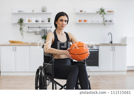 Caucasian female in wheelchair posing with basketball in open-plan kitchen. 111515081