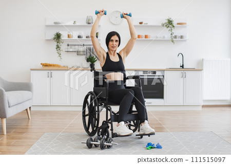 Woman in wheelchair lifting weights while exercising with limited mobility. 111515097