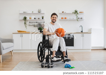 Adult in wheelchair holding basketball in room interior Adult in wheelchair holding basketball in room interior 111515107