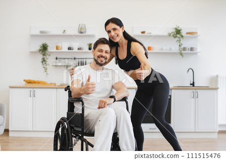 Female physiotherapist or wife helping young man in wheelchair doing workout. 111515476