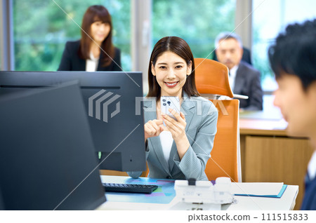 一位年輕的女商人在辦公室看智能手機 一位年輕的女商人在辦公室看智能手機 111515833