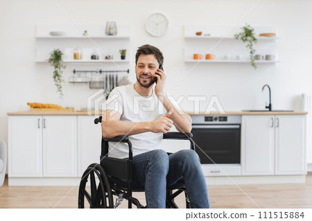 Male with mobility impairment speaking on mobile in kitchen Male with mobility impairment speaking on mobile in kitchen 111515884