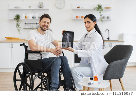 Female nurse and mature man wheelchair user, showing x-ray scan of spine. 111516087