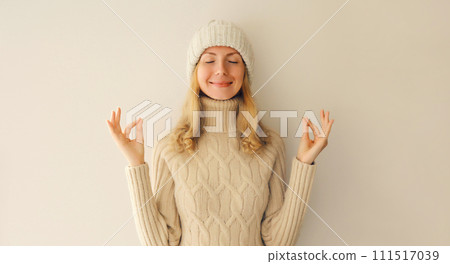 Relaxed happy young woman meditates in yoga position in winter warm knitted sweater and hat 111517039