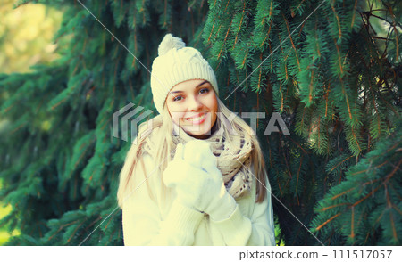 Winter portrait of happy smiling young woman in hat, scarf in forest on christmas tree background Winter portrait of happy smiling young woman in hat, scarf in forest on christmas tree background 111517057