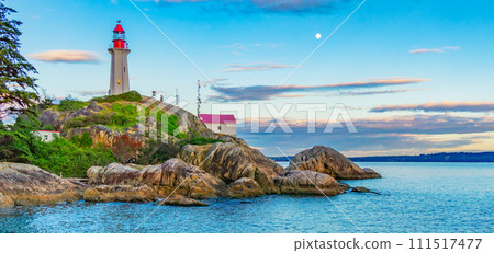 Lighthouse on a rocky coast during a cloudy sunset. 111517477