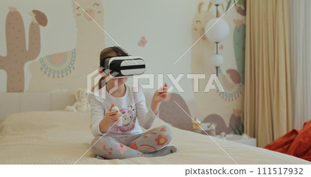 Girl kid child schoolgirl playing online video game in 3D world metaverse using virtual reality helmet at home. Girl kid child schoolgirl playing online video game in 3D world metaverse using virtual reality helmet at home. 111517932