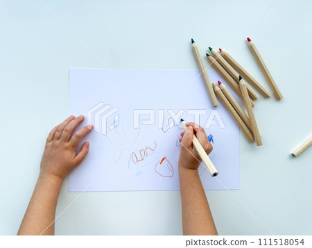 small child draws with colored pencils on paper on white table. 111518054