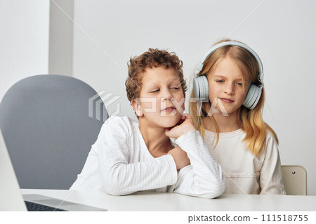 Happy Caucasian boy and girl playing and studying together at home with their laptops They are sitting at a table in the living room, wearing headphones and using technology for elearning The room is Happy Caucasian boy and girl playing and studying together at home with their laptops They are sitting at a table in the living room, wearing headphones and using technology for elearning The room is 111518755