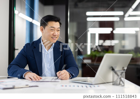 Satisfied with achievement male financier accountant inside office at workplace, Asian businessman smiling happy working with accounts contracts and reports, using laptop. 111518843