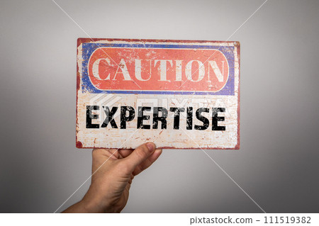 Expertise Concept. Metal warning sign in a woman's hand on a white background Expertise Concept. Metal warning sign in a woman's hand on a white background 111519382