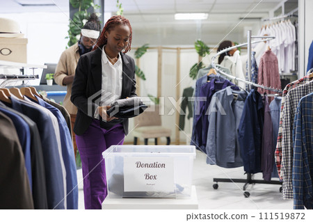 Shopping mall african american customer putting clothes in donation box to help poor. Woman contributing to charity volunteering organization, giving apparel for humanitarian aid 111519872