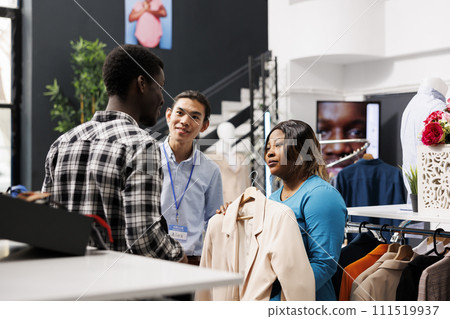 African american woman wanting to buy simple shirt, asking modern boutique manager about fabric. Stylish couple looking at hangers with new collection, shopping for trendy clothes in retail store 111519937