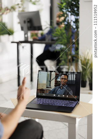 Executive on laptop screen listening to employee presentation through video call. Project manager having online meeting with african american colleague in coworking space 111519952