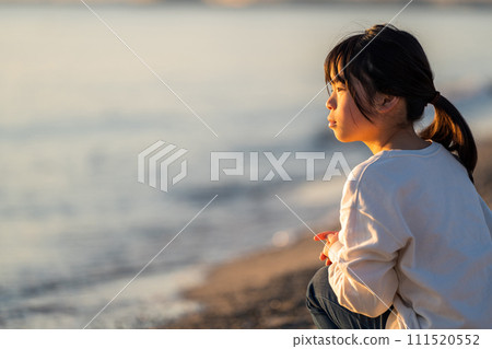 日落時分，一個女孩站在海灘上。 111520552