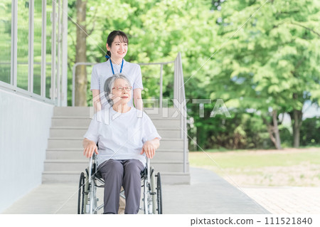 Elderly people in wheelchairs and caregivers (helpers) walking in the park Elderly people in wheelchairs and caregivers (helpers) walking in the park 111521840