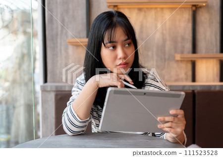 A serious Asian woman is using her digital tablet, thinking and planning her work in her head. A serious Asian woman is using her digital tablet, thinking and planning her work in her head. 111523528