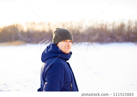 man in winter clothes on frozen snow lake, winter walk. looking at the camera European Caucasian young adult man in knitted hat. portrait 111523883