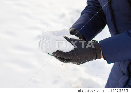 pile of snow in hands after heavy snowfall. man in gloves and winter clothes takes snow in his hands. leisure activities, snowball fight game 111523885