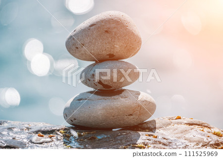 Balanced rock pyramid on sea pebbles beach, sunny day and clear sky at sunset. Golden sea bokeh on background. Selective focus, zen stones on sea beach, meditation, spa, harmony, calm, balance concept Balanced rock pyramid on sea pebbles beach, sunny day and clear sky at sunset. Golden sea bokeh on background. Selective focus, zen stones on sea beach, meditation, spa, harmony, calm, balance concept 111525969