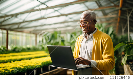 A dark-skinned African American man with a gadget, laptop, tablet is planting and caring for plants, seedlings, vegetables in a greenhouse. A dark-skinned African American man with a gadget, laptop, tablet is planting and caring for plants, seedlings, vegetables in a greenhouse. 111526446