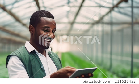 A dark-skinned African American man with a gadget, laptop, tablet is planting and caring for plants, seedlings, vegetables in a greenhouse. A dark-skinned African American man with a gadget, laptop, tablet is planting and caring for plants, seedlings, vegetables in a greenhouse. 111526452