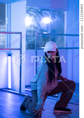 Active young woman moving in hip hop dance in dance hall with purple neon lights Active young woman moving in hip hop dance in dance hall with purple neon lights 111526465