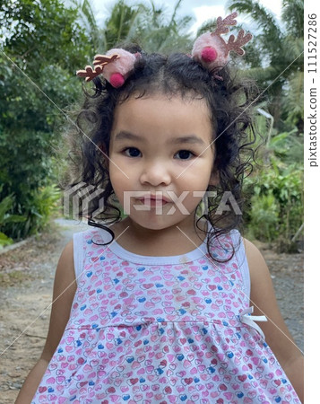 Portrait of cute little girl with curly hair in garden. Happy childhood 111527286