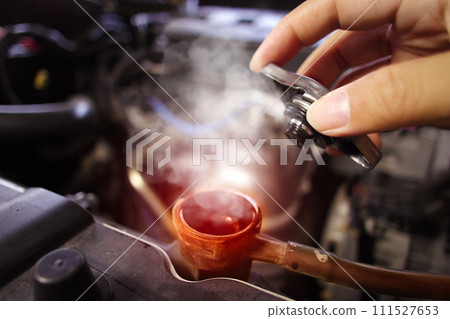 Hand opens the radiator cap with steam escaping around the engine compartment from the high heat 111527653