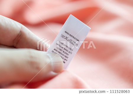 Hand hold and reading at white laundry care washing instructions clothes label on pink shirt Hand hold and reading at white laundry care washing instructions clothes label on pink shirt 111528063