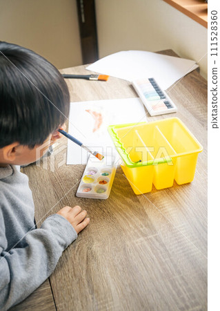 A boy drawing on white paper using paints 111528360