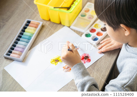 A boy drawing on white paper using paints 111528400