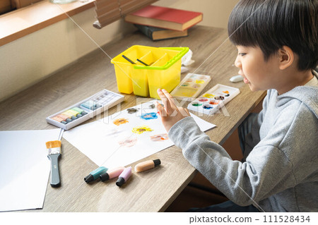 A boy drawing on white paper using paints A boy drawing on white paper using paints 111528434