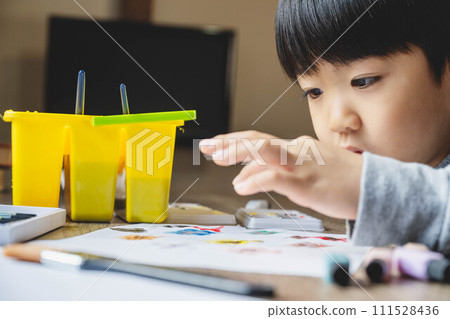 A boy drawing on white paper using paints A boy drawing on white paper using paints 111528436