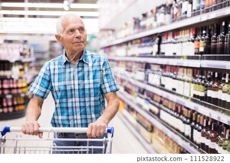 Elderly retired senor buying wine in the alcohol section of the supermarket Elderly retired senor buying wine in the alcohol section of the supermarket 111528922
