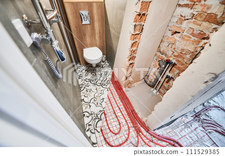 Old apartment restroom with underfloor heating pipes and new renovated toilet room with electric towel dryer. Comparison of washroom lavatory with wall-hung flush toilet before and after renovation. 111529385