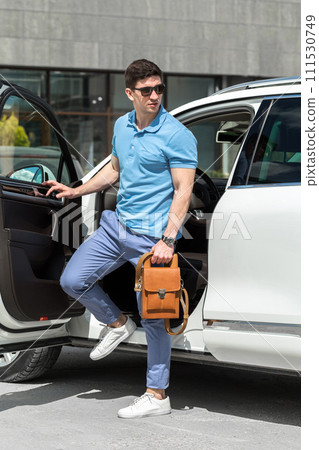 Young man with brown leather bag standing near the car 111530749