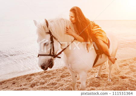 A woman in a dress stands next to a white horse on a beach, with the blue sky and sea in the background. A woman in a dress stands next to a white horse on a beach, with the blue sky and sea in the background. 111531364