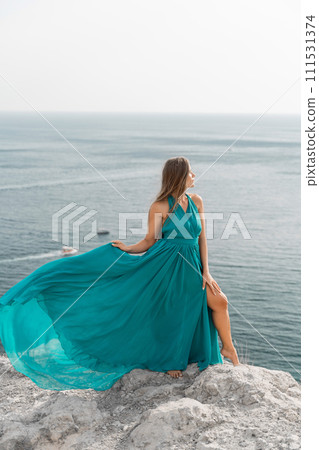 Woman sea trevel green dress. Side view a happy woman with long hair in a long mint dress posing on a beach with calm sea bokeh lights on sunny day. Girl on the nature on blue sky background. 111531374