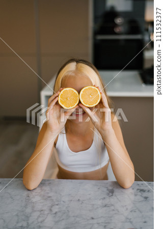 Child holding orange slice in front of her eyes at the kitchen table Child holding orange slice in front of her eyes at the kitchen table 111532377