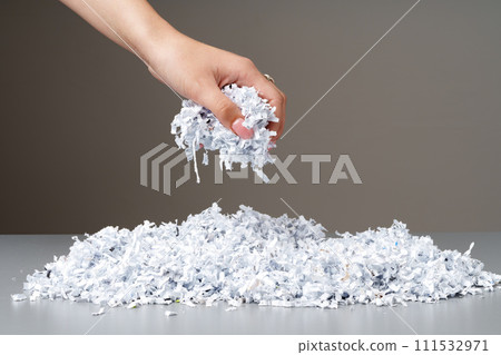 Hand holding a bunch of shredded paper against gray background Hand holding a bunch of shredded paper against gray background 111532971