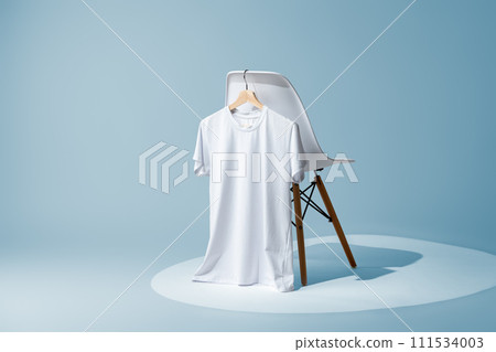 White blank t-shirt hanging on chair against blue wall White blank t-shirt hanging on chair against blue wall 111534003