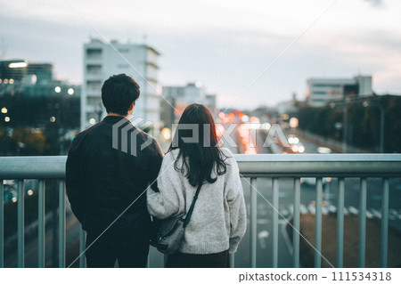Couple looking at the city from a pedestrian bridge at sunset Couple looking at the city from a pedestrian bridge at sunset 111534318