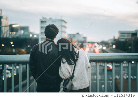日落時,一對夫婦靠在肩膀上,從人行天橋上眺望城市 日落時,一對夫婦靠在肩膀上,從人行天橋上眺望城市 111534319