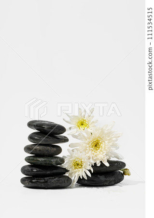 Stacked black spa stones with flowers on white background Stacked black spa stones with flowers on white background 111534515