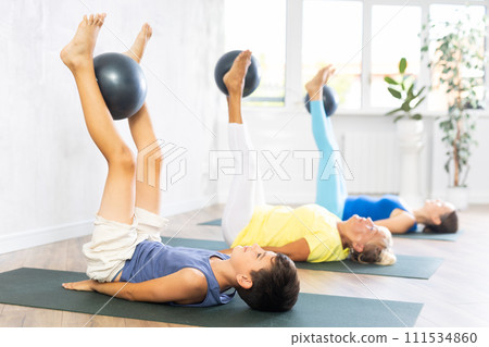 Mom, grandmother and teen grandson performing exercises with softball lying on floor Mom, grandmother and teen grandson performing exercises with softball lying on floor 111534860