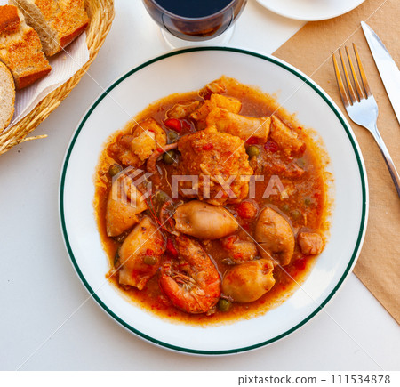 Catalan cuisine zarzuela with shrimp served on white plate on wooden table 111534878