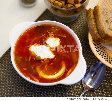 Delicious meat soup solyanka on broth served with sour cream and herbs Delicious meat soup solyanka on broth served with sour cream and herbs 111535023