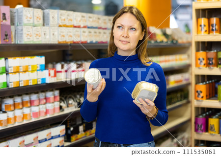 Young woman choosing canned food for dog at pet store 111535061